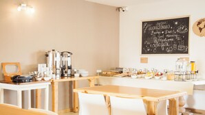 A café with wooden tables and white chairs, a chalkboard with greetings, and various food and drink items on display.