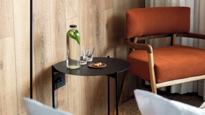 A modern room with a wooden wall, a black floor lamp, a round table with a glass bottle, glasses, and a plate.