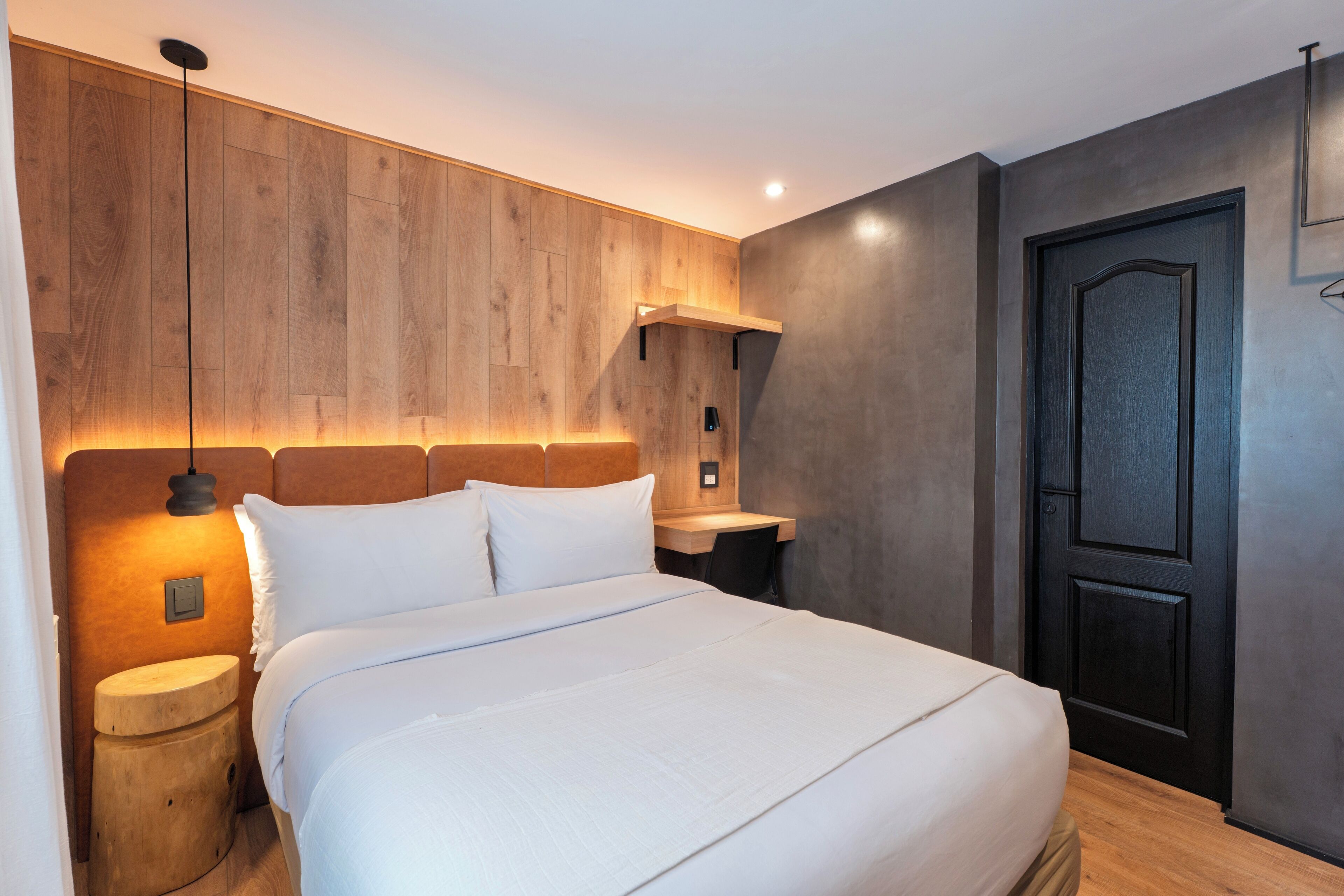 Une chambre à coucher moderne avec une tête de lit en bois, une table de chevet, un bureau et une porte.