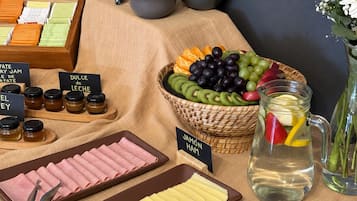 Una mesa de buffet con diversos alimentos, como carnes frías, quesos, frutas y una jarras de bebidas.