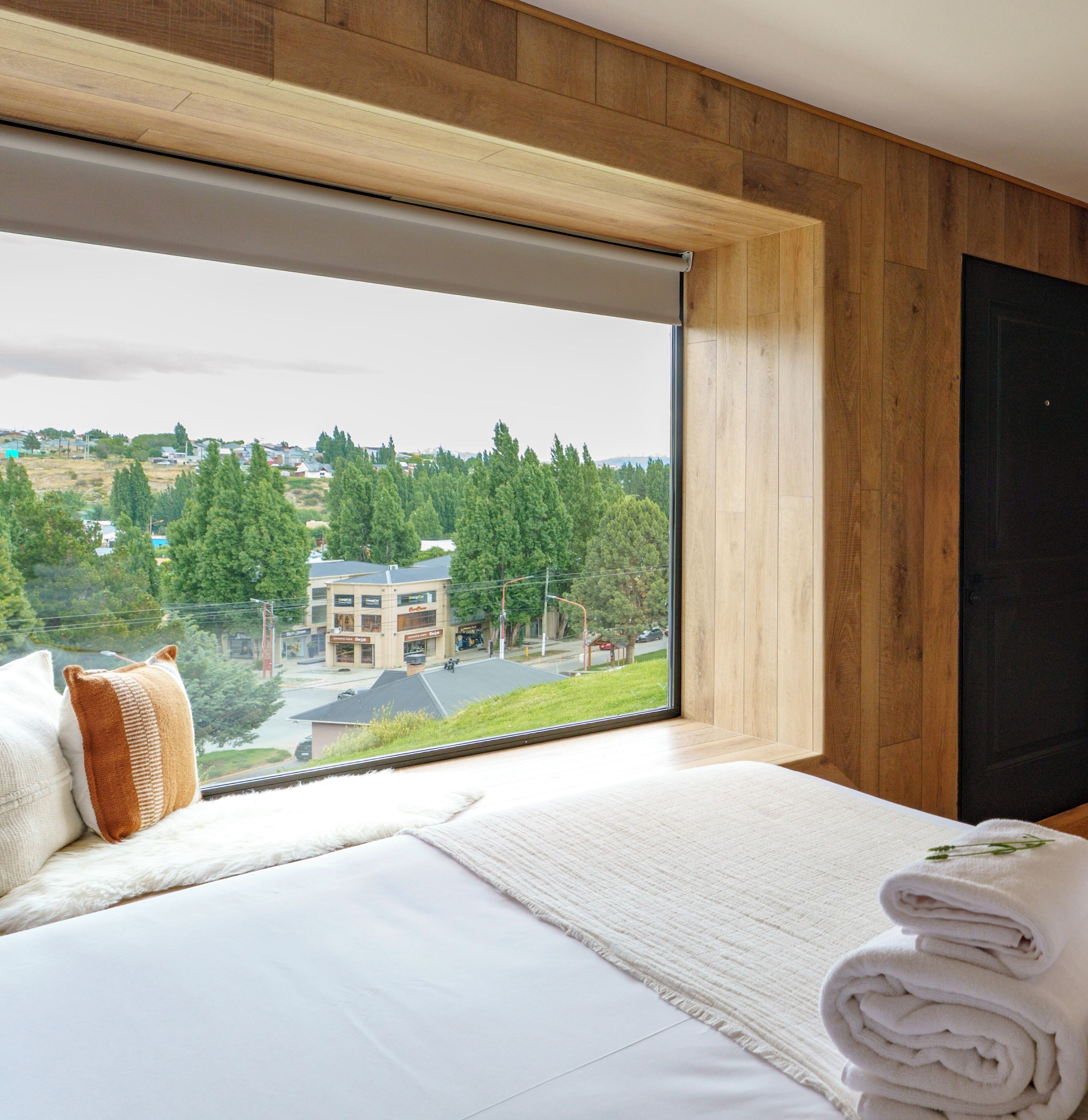 A hotel room with a large window offering a view of a town and greenery.