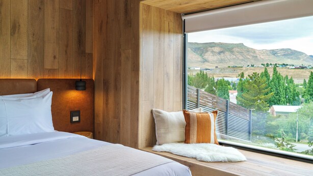 A bedroom with a large bed, wooden paneling, a view of mountains, and a window with a view of a town.