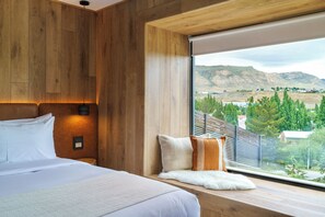 A bedroom with a large bed, wooden paneling, a view of mountains, and a window with a view of a town.
