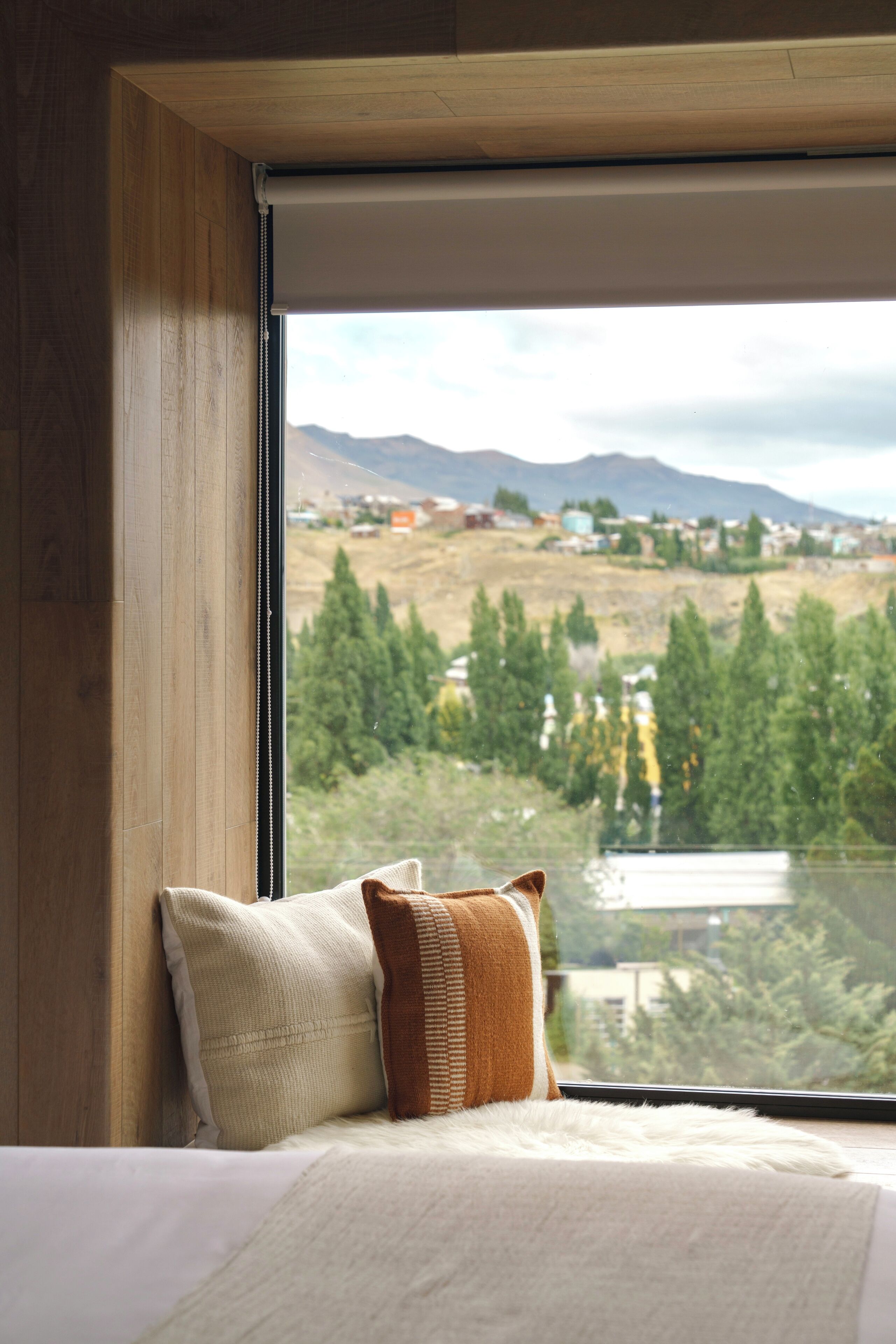 A bedroom with a large window, wooden walls, and a bed with pillows.