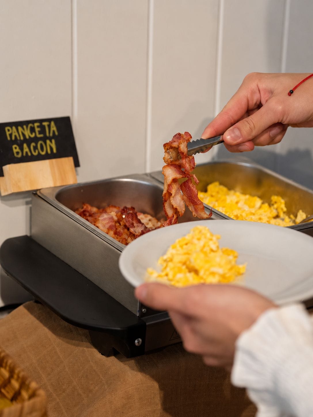 Un buffet de petit-déjeuner avec une pancarte indiquant « PANCTA BACON » et des œufs brouillés.