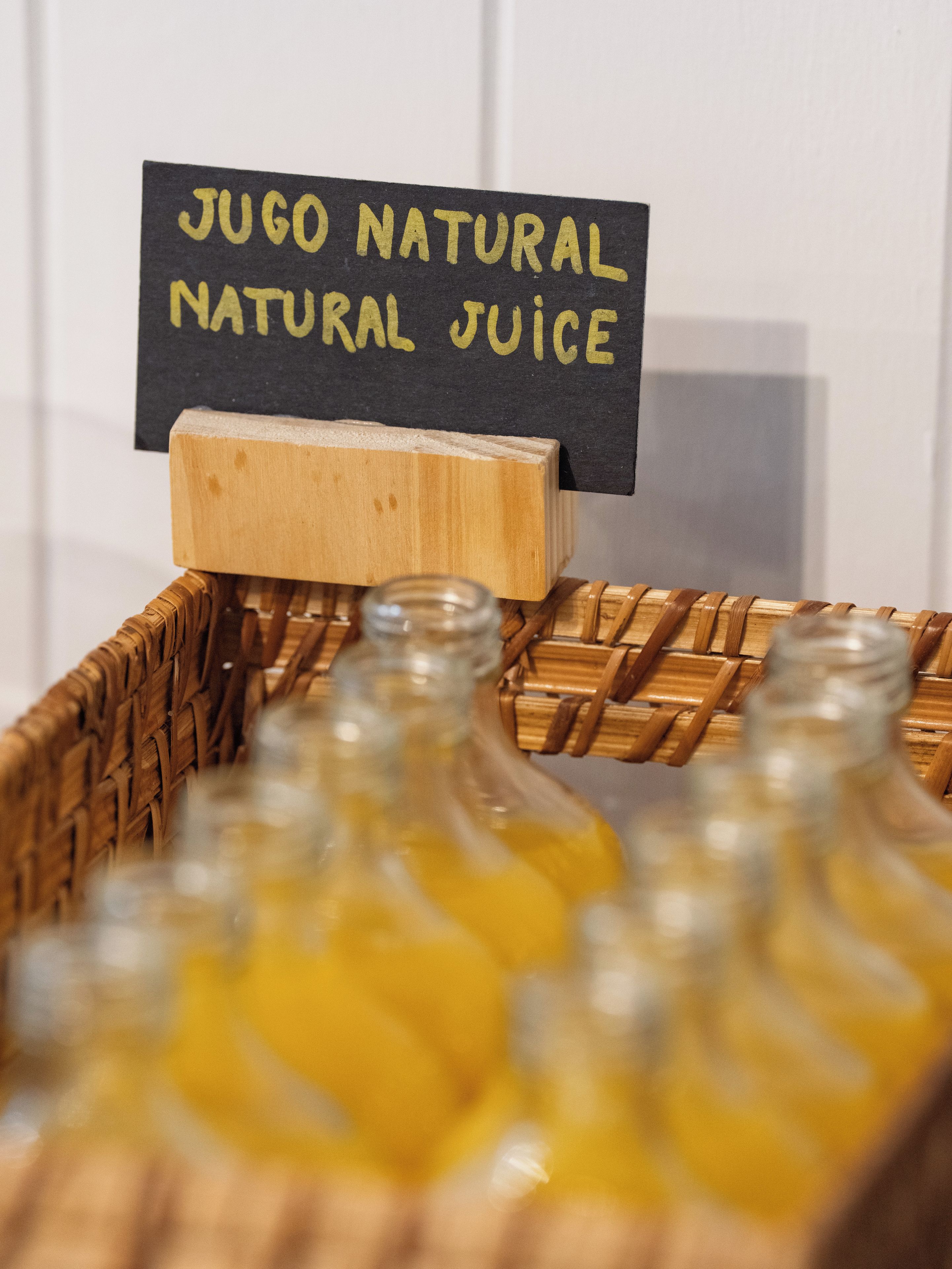 Una caja de madera con un letrero que dice 'JUGO NATURAL JUICE' y varias botellas de vidrio con jugo.