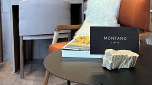A modern hotel room with a dark blue accent wall, a wooden desk, a comfortable chair, and a small table with a book and a stone.