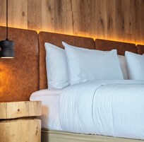 Ein ordentlich bezogenes Bett mit weißen Leinen und Kissen, ein Holz-Kopfteil und eine hängende Pendelleuchte.