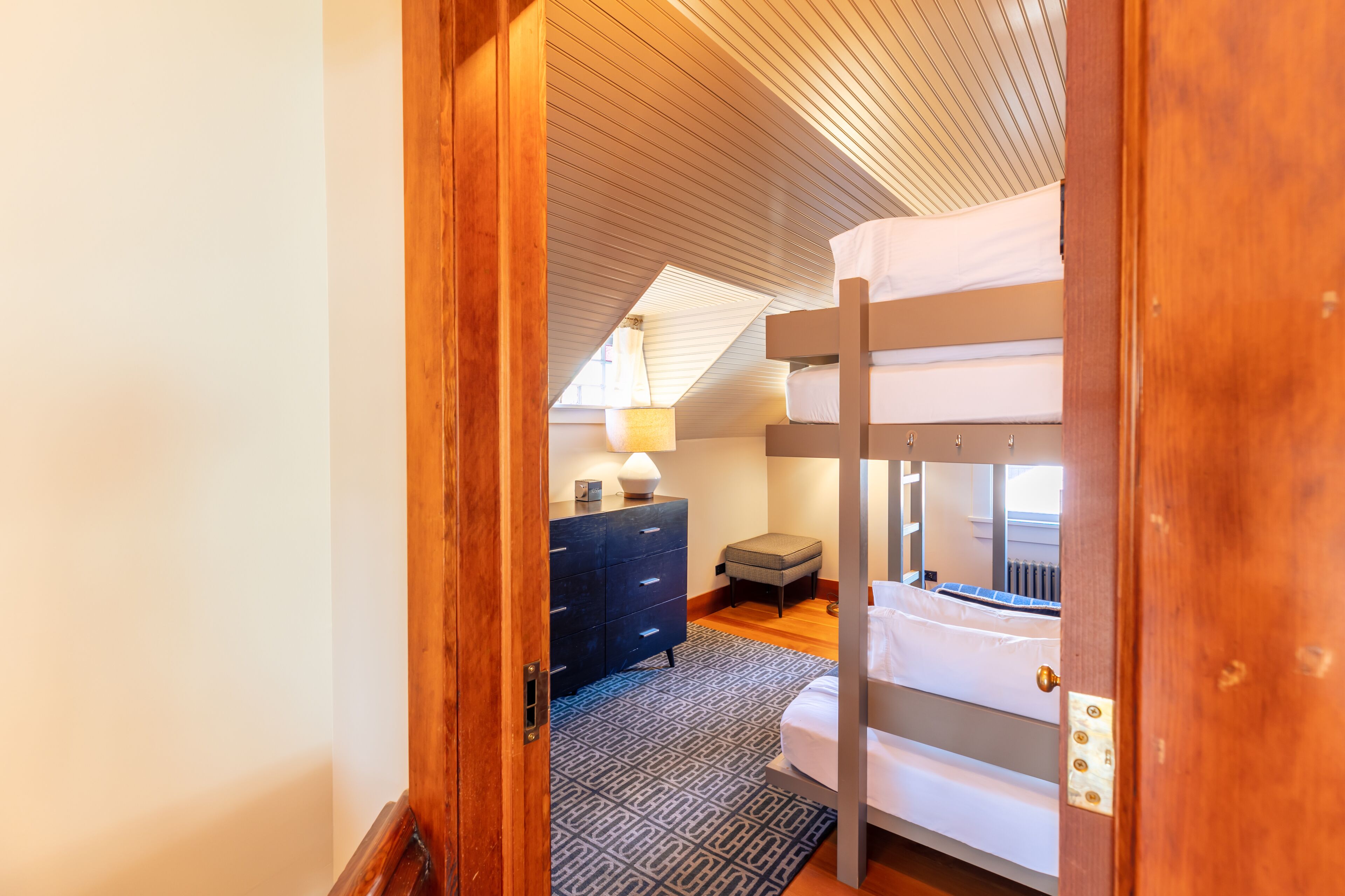 A bedroom with a bunk bed, a dresser, a lamp, and a patterned rug.