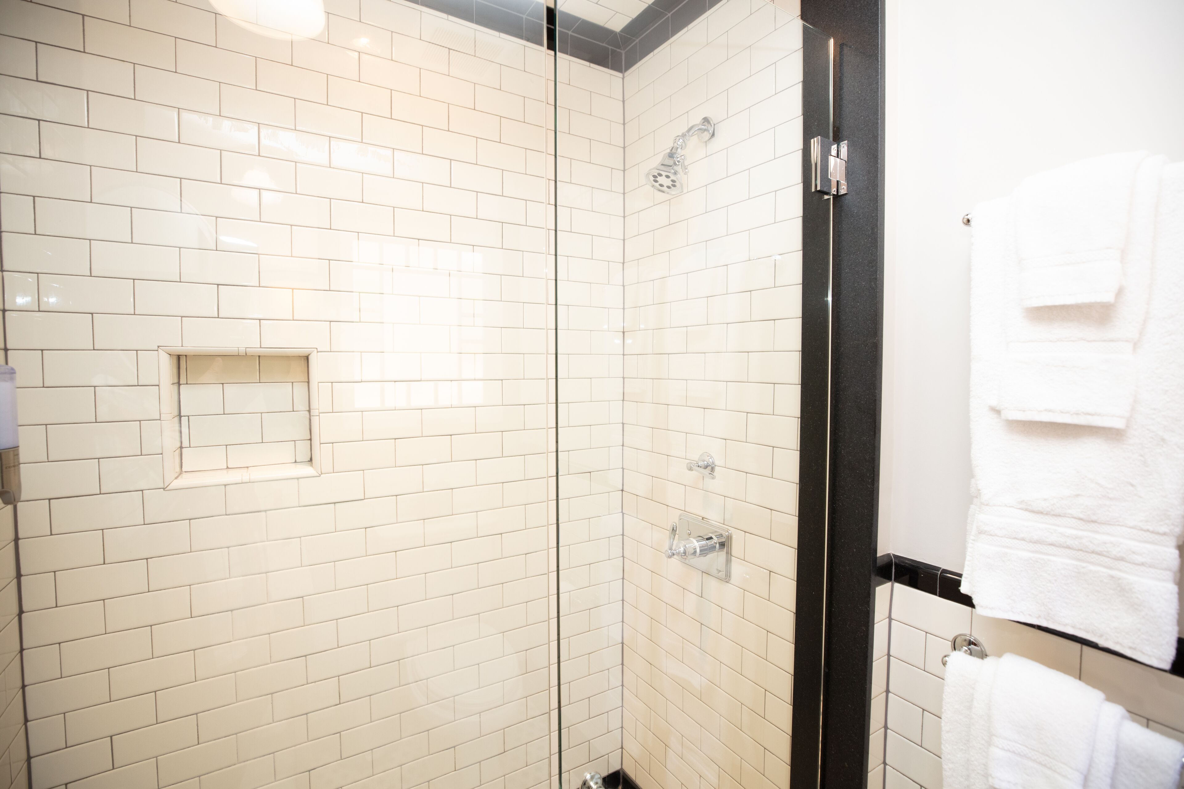 A bathroom with white subway tiles, a glass shower enclosure, and a towel rack with folded towels.