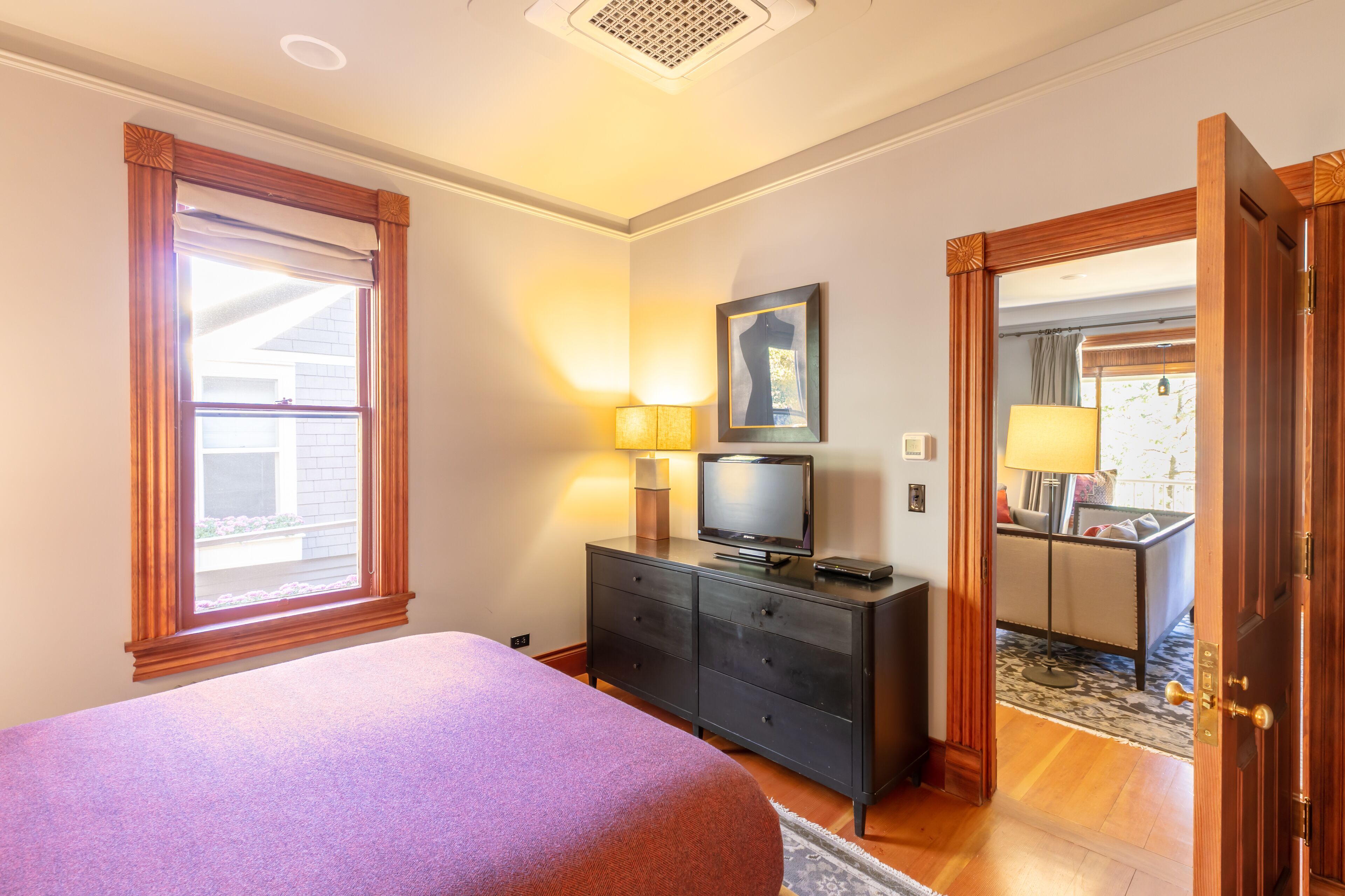A bedroom with a bed, a dresser, a television, and a window with curtains.