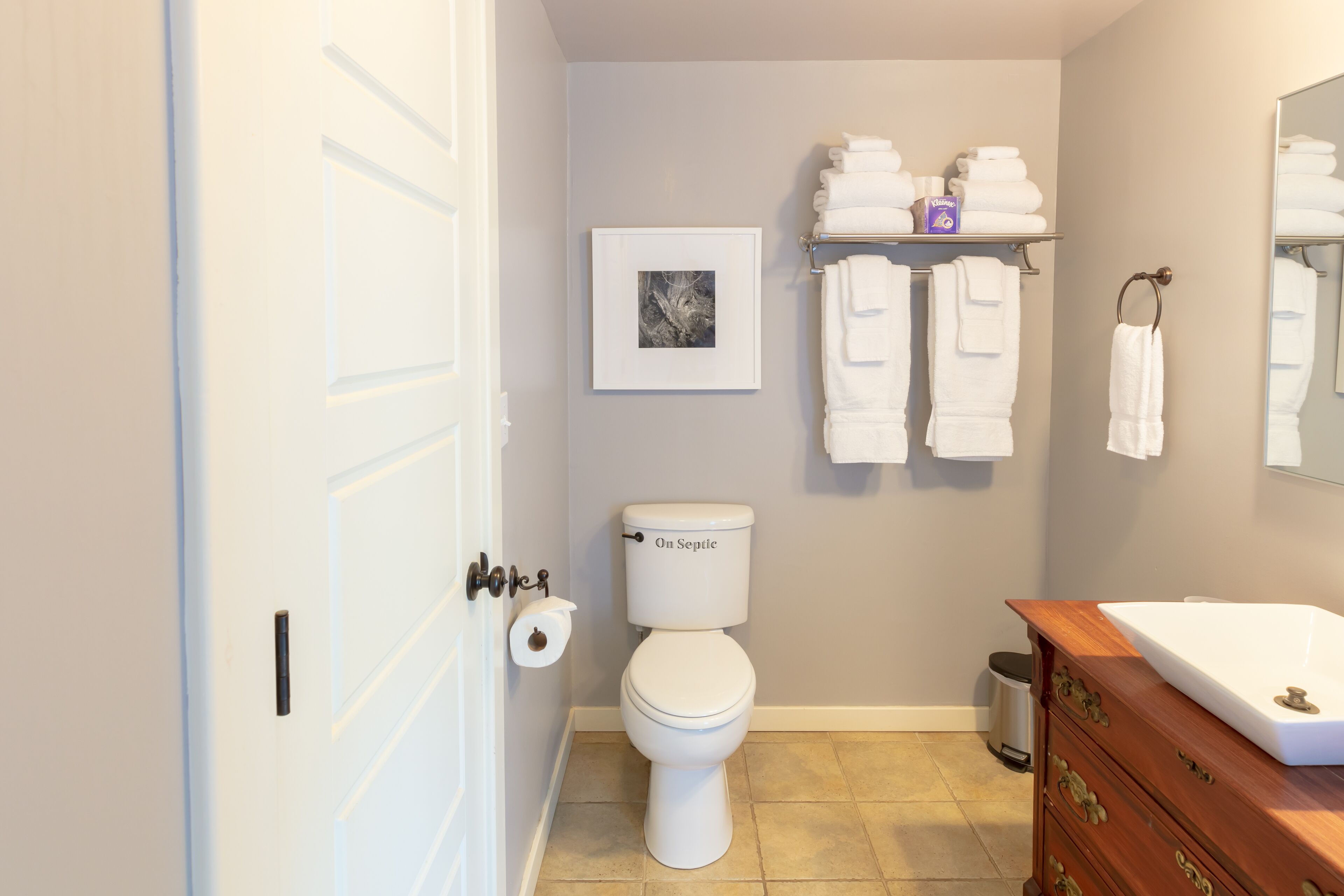 A bathroom with a toilet, a sink, a vanity, towels, and a framed picture on the wall.