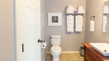 A bathroom with a toilet, a sink, a vanity, towels, and a framed picture on the wall.