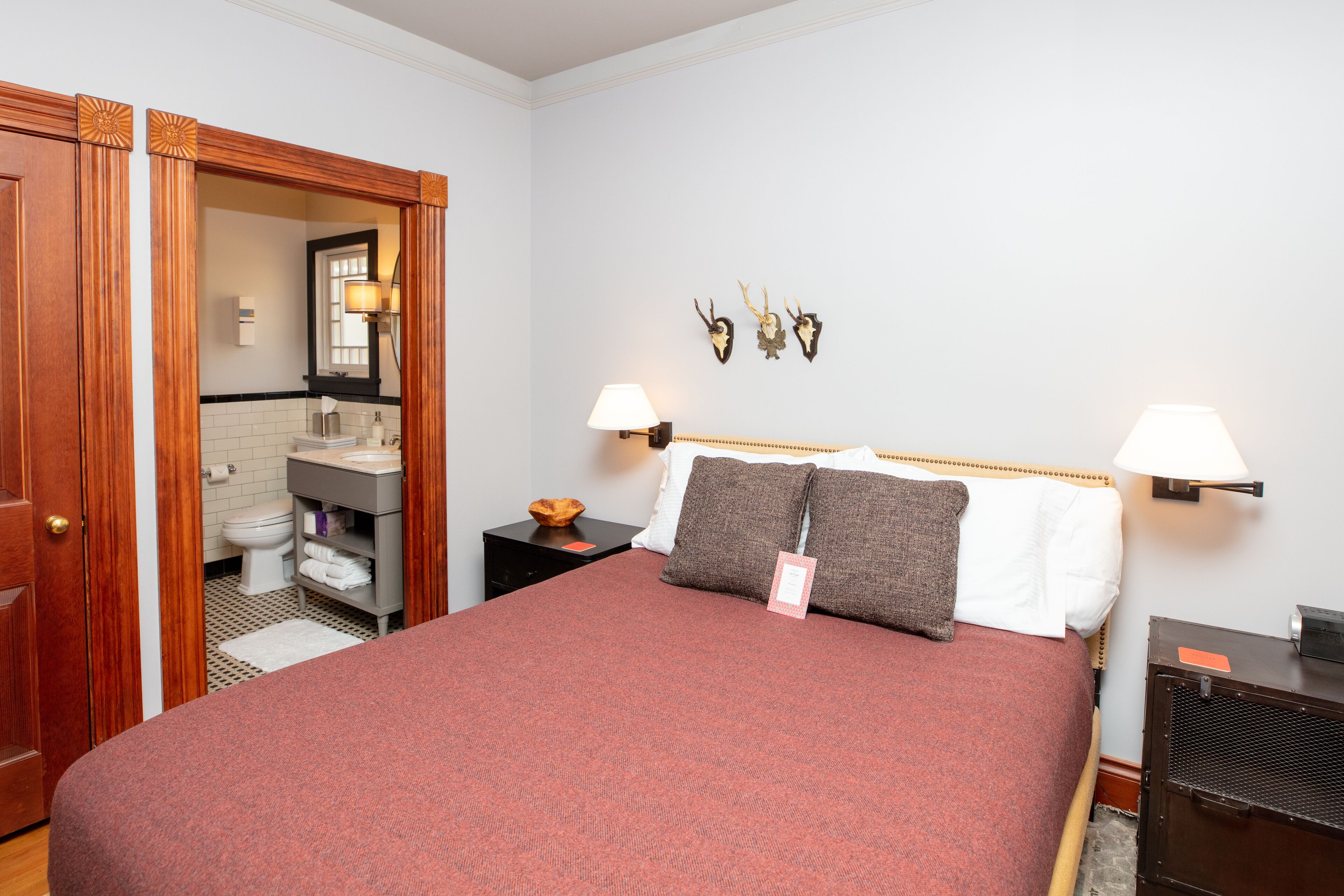 Une chambre d’hôtel avec un grand lit, deux lampes de chevet, une tête de lit en bois, une petite table avec un bol, et un miroir fixé au mur.