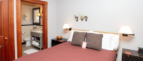 Une chambre d’hôtel avec un grand lit, deux lampes de chevet, une tête de lit en bois, une petite table avec un bol, et un miroir fixé au mur.