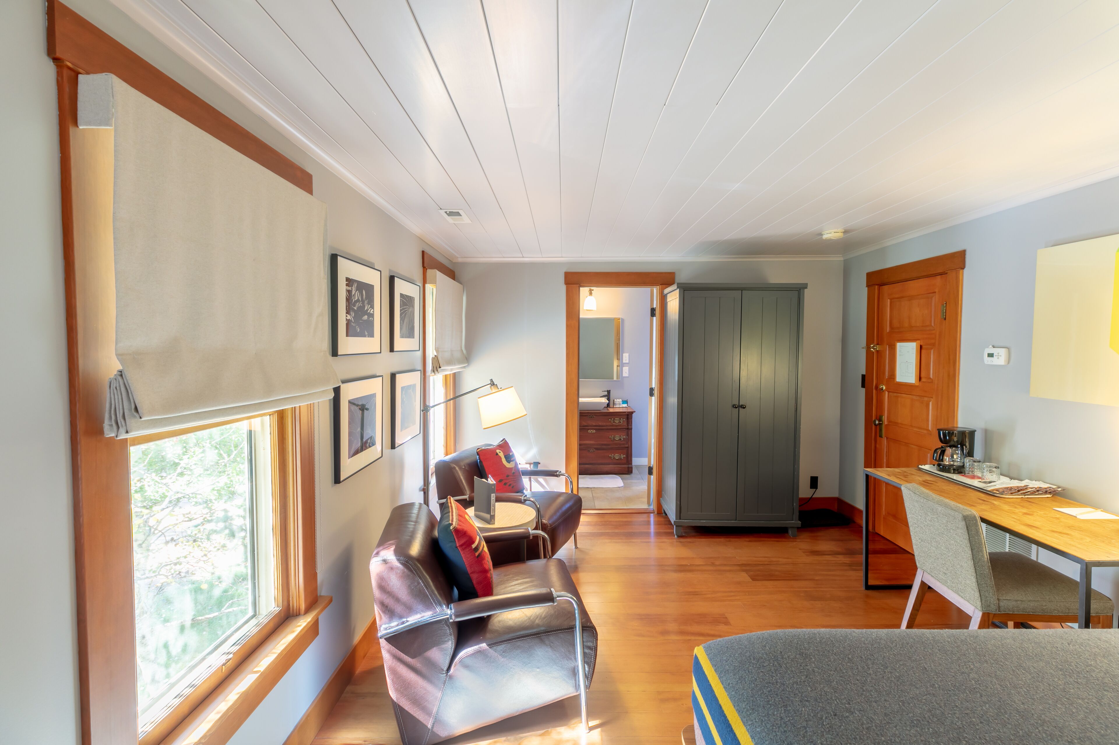 A spacious room with a wooden floor, a leather sofa, a dining table, and a large window.
