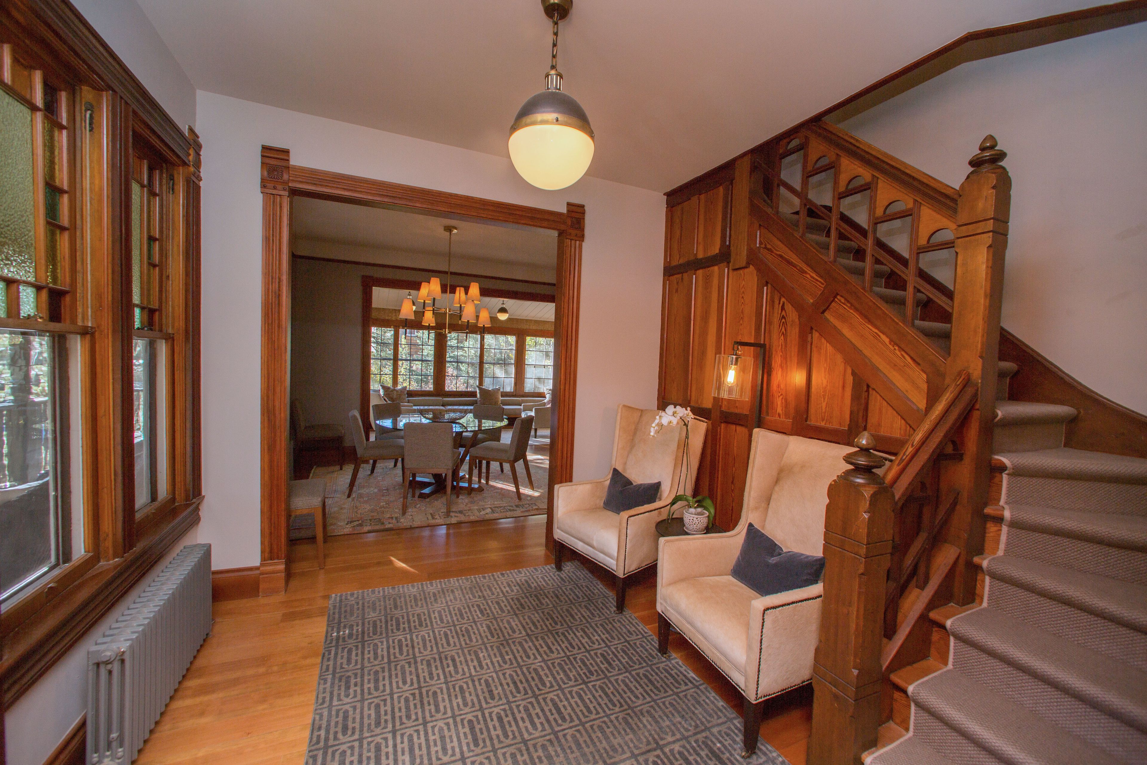 Un vaste salon agrémenté d’un escalier en bois, d’un coin repas et offrant une vue sur l’extérieur grâce à une porte ouverte.