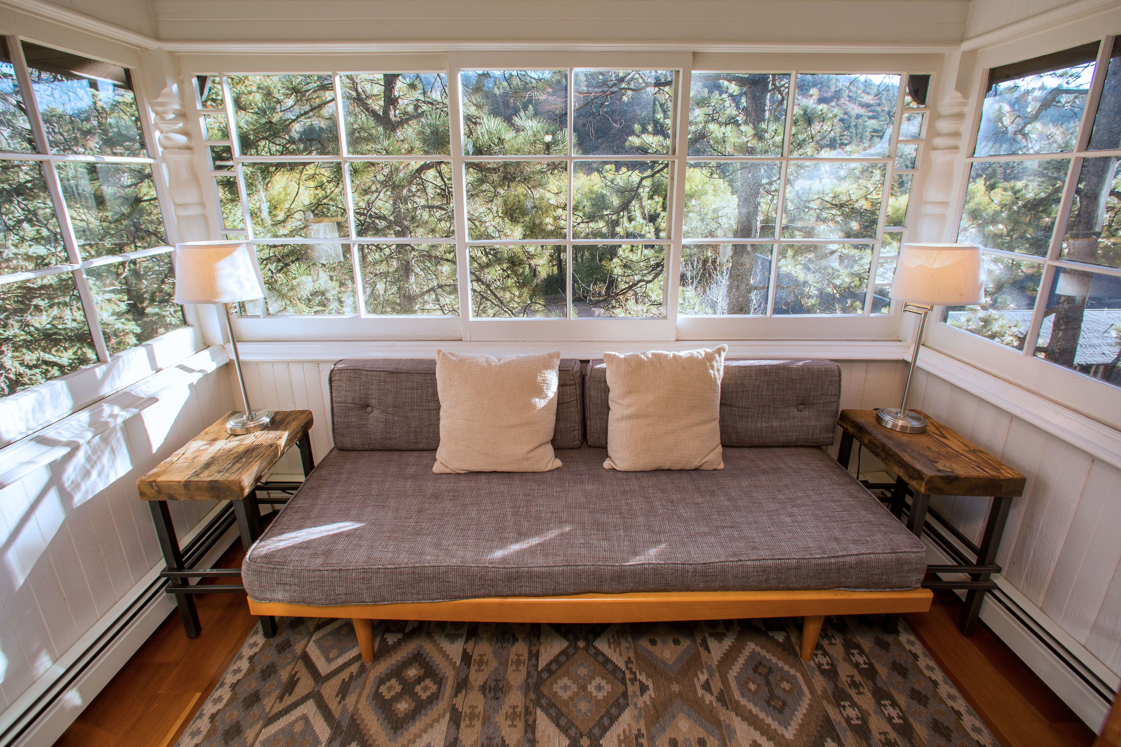 A bedroom with a large window, a bed, two nightstands, and a patterned rug.