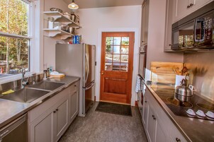 A compact kitchen with stainless steel appliances, a wooden door, and a view of the outdoors.