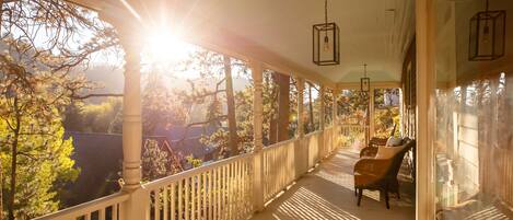 A covered porch with a wooden railing, a bench, and hanging lanterns.