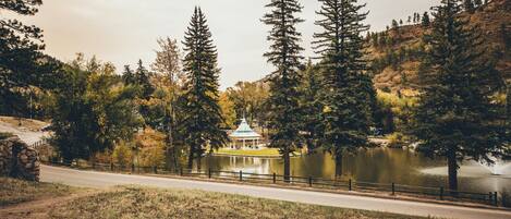 A gazebo by a lake surrounded by tall trees and a stone wall.