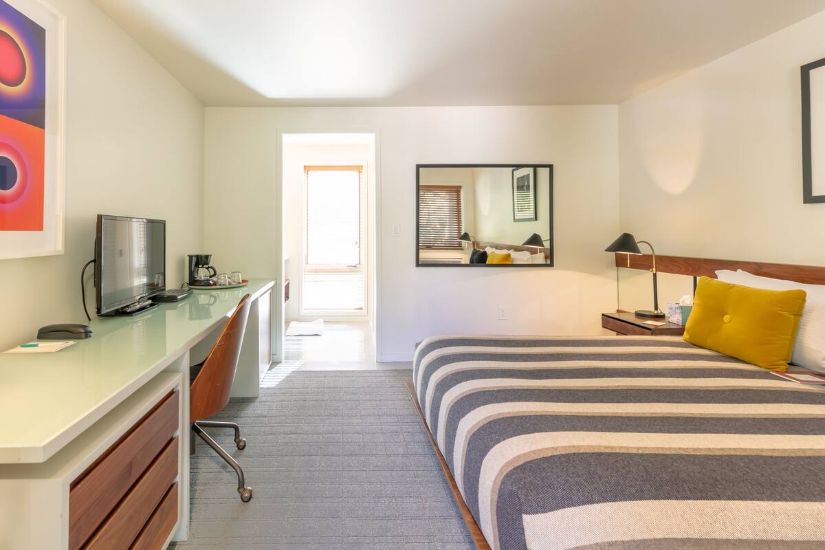 A hotel room with a bed, a desk, a chair, a television, and a mirror.