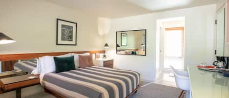 Habitación de hotel con una cama grande, mesitas de noche, un escritorio, una silla, un espejo y una ventana con persianas.