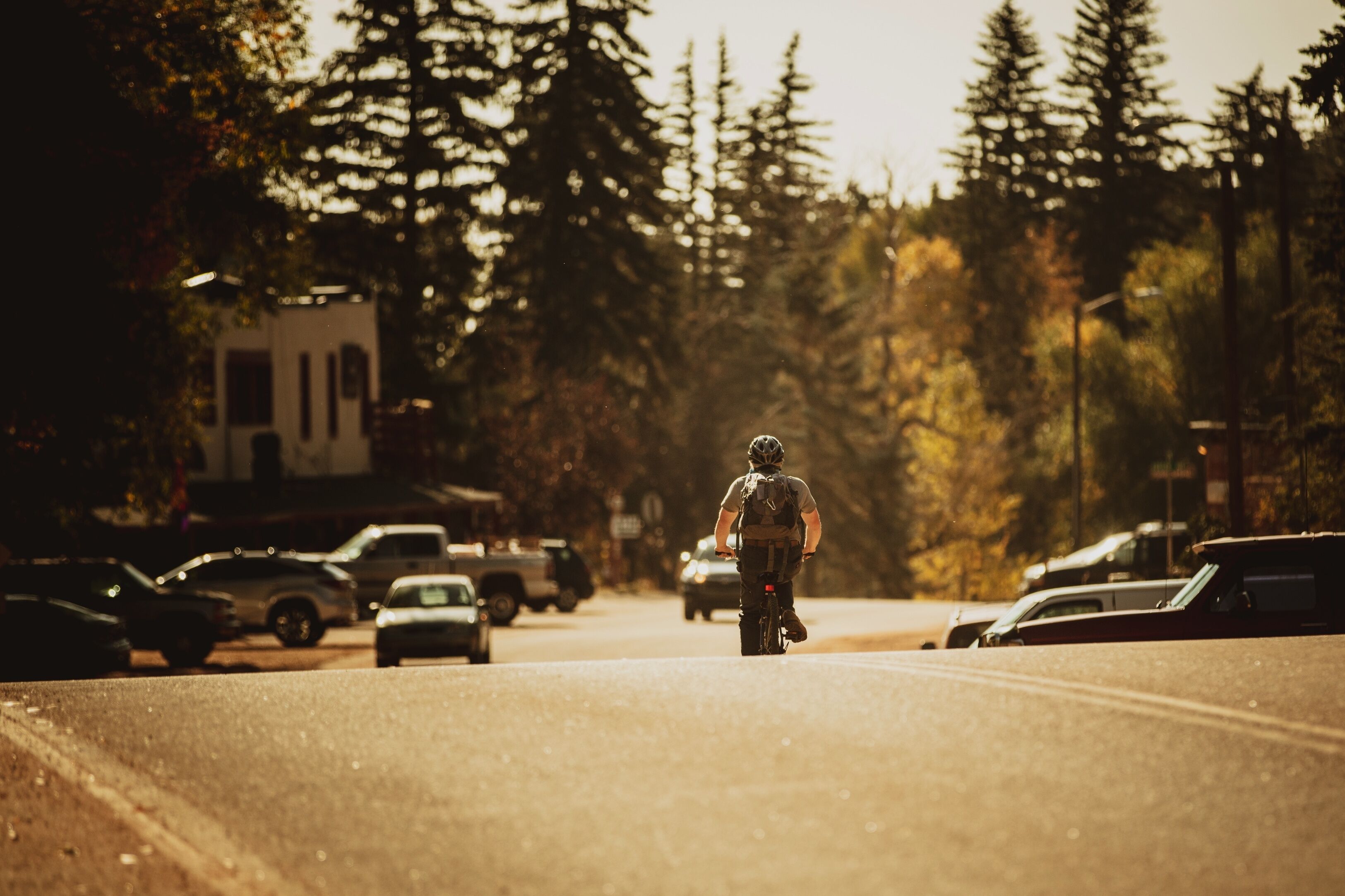 A person riding a bicycle on a road with cars parked on the side.