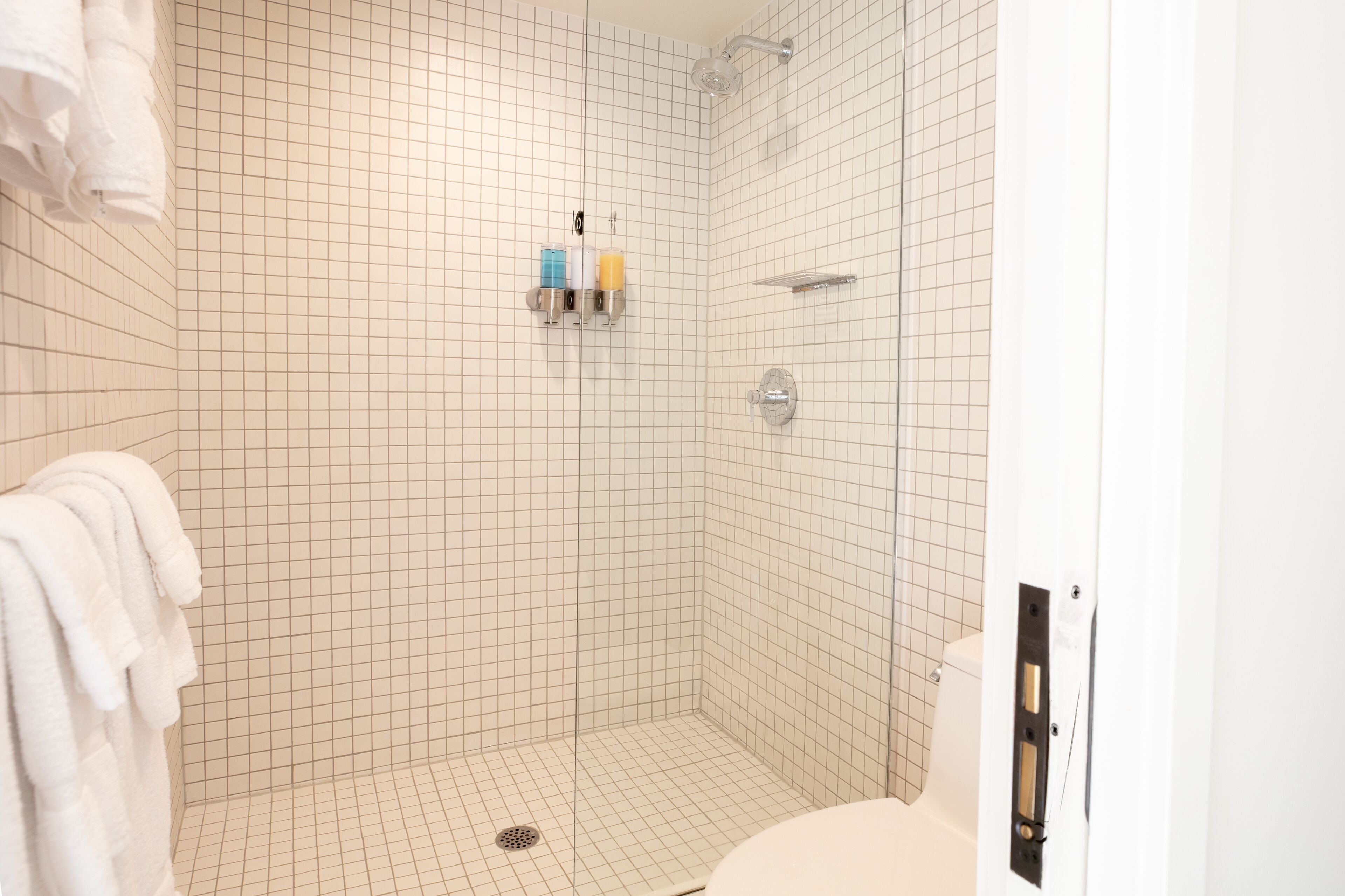 Um chuveiro revestido com azulejos, um chuveiro manual, um vaso sanitário e um porta-toalhas com toalhas.
