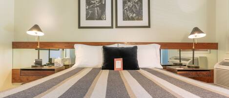 A hotel room with a large bed, two bedside tables, a nightstand, a desk, and two framed pictures on the wall.