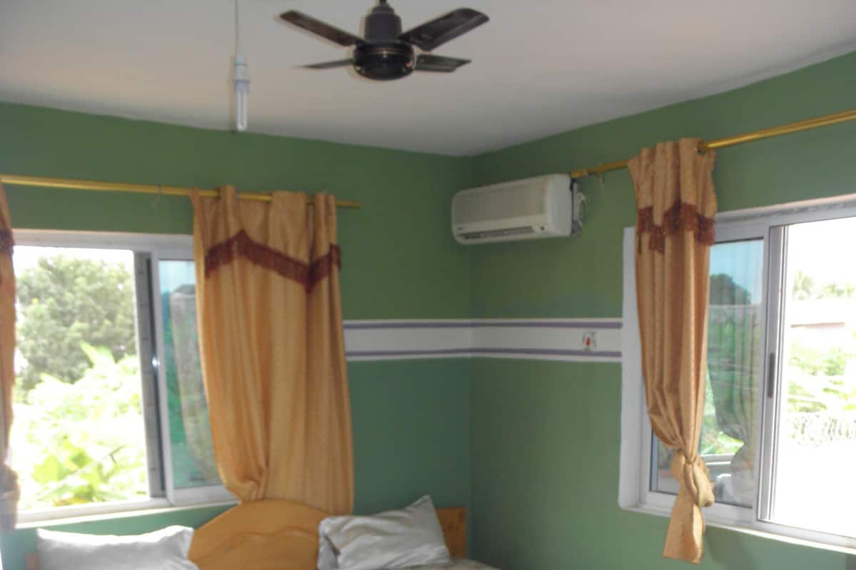 A bedroom with a bed, curtains, an air conditioning unit, and a window.