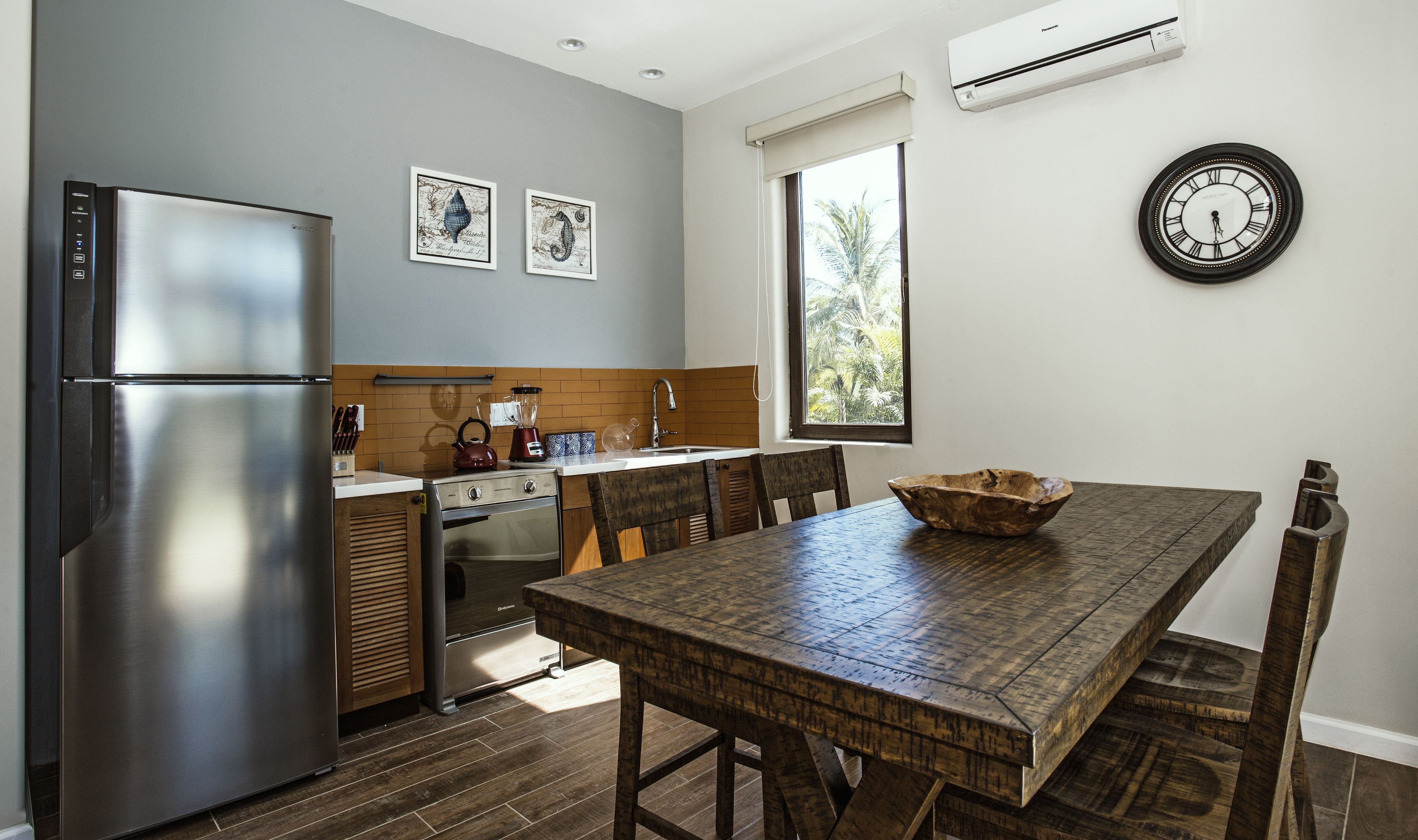Une cuisine moderne avec un réfrigérateur en acier inoxydable, une table à manger en bois et une horloge au mur.