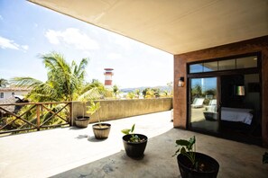 Ein Balkon mit Topfpflanzen, Blick auf einen Leuchtturm und ein Einblick in einen Raum mit einem Bett und einem Fenster.