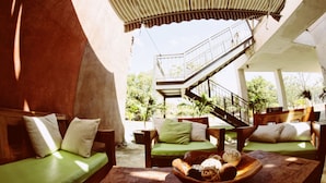 A sunlit outdoor seating area with green cushioned sofas, a wooden table with a bowl of snacks, and a staircase leading to an upper level. - El Sitio Villas (Las Escobas del Venado)