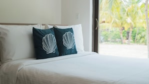 A bed with white and teal pillows, a view of palm trees through a window. - El Sitio Villas (Las Escobas del Venado)