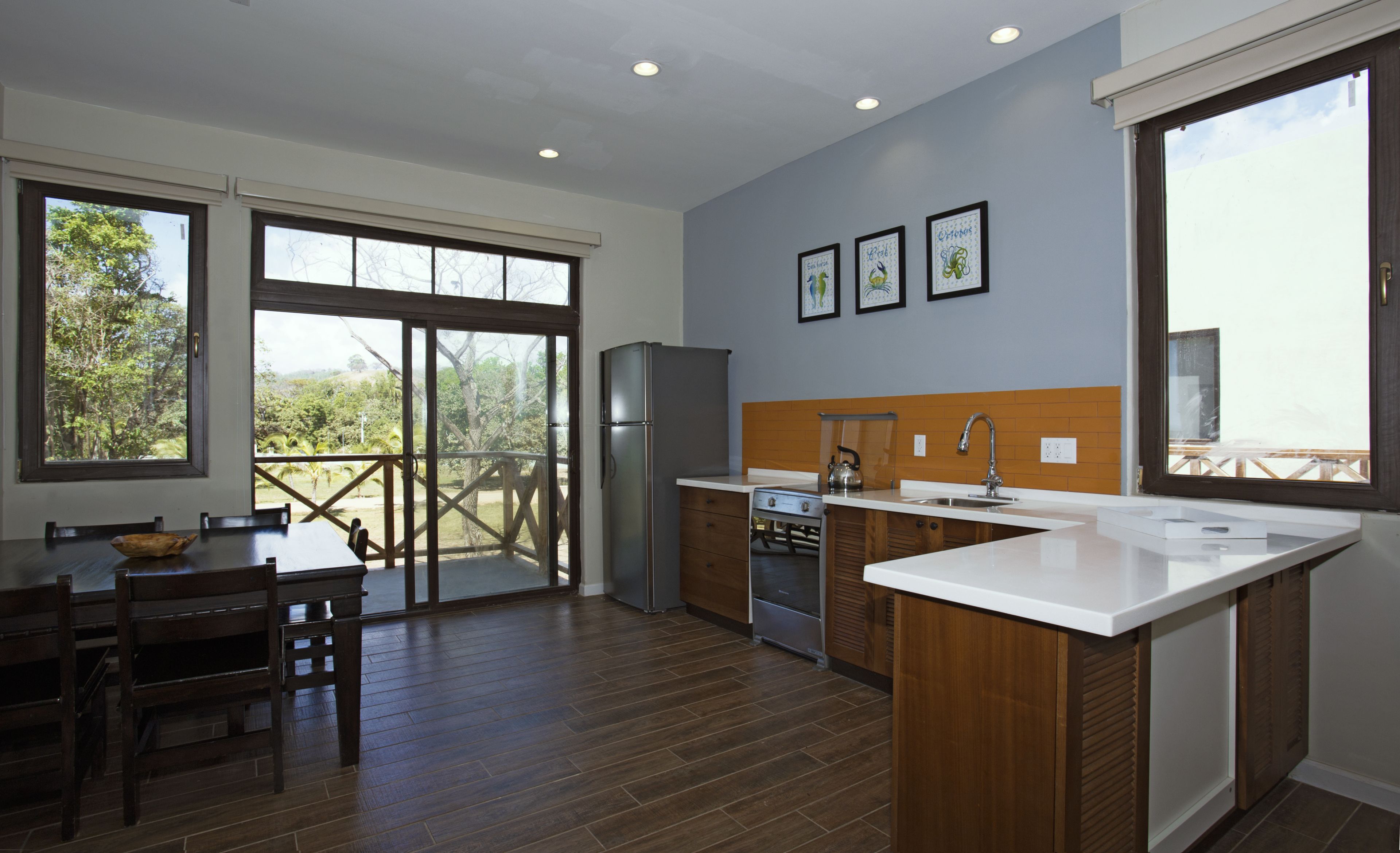 A modern kitchen with a large island, wooden cabinetry, and a view of the outdoors through large windows.