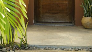 A wooden door with a metal handle, a potted plant to the right, and a small sign on the wall. - El Sitio Villas (Las Escobas del Venado)