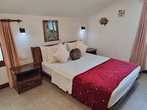 Ein ordentlich eingerichtetes Schlafzimmer mit Bett, Nachttischen, einer Wandleuchte und einem Gemälde.