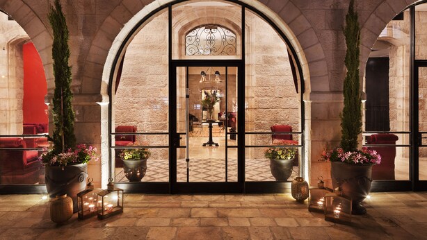 An arched entrance with a tiled floor, potted plants, and a seating area with red chairs. - Villa Brown Jerusalem (Jerusalem)