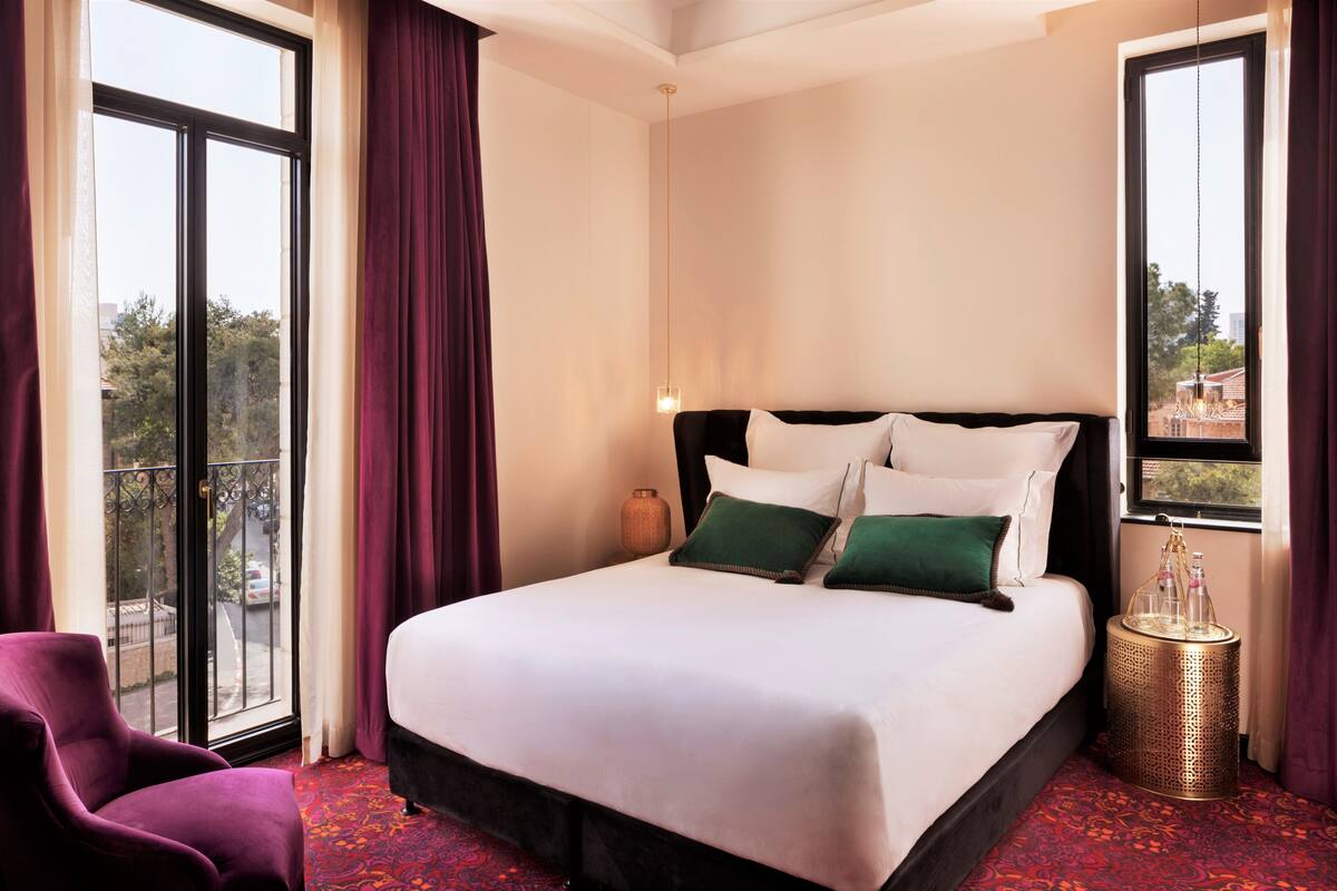 A hotel room with a large bed, a chair, a small table, and a view of the outside.