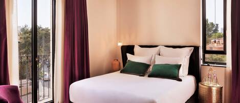 A hotel room with a large bed, a chair, a small table, and a view of the outside.
