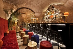 A bar area with a checkered floor, red velvet seating, and a variety of stools.