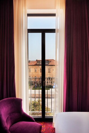 A hotel room with a large window, a purple armchair, and a white bed.