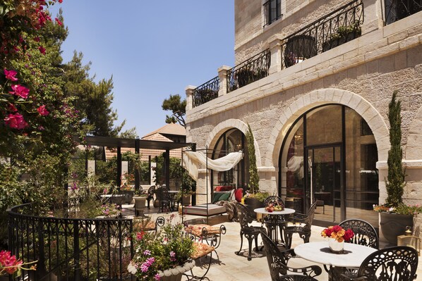 An outdoor patio with tables and chairs, surrounded by potted plants and flowers.