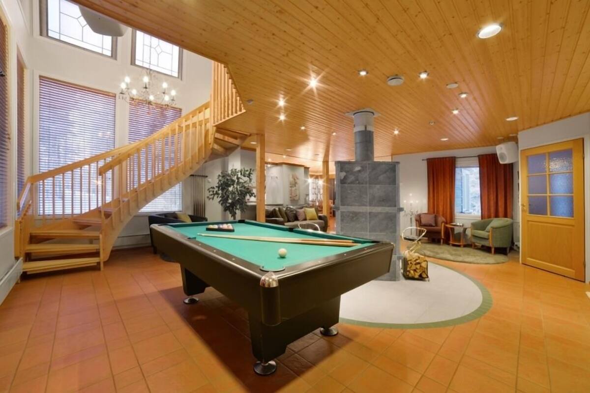 Une pièce spacieuse équipée d’une table de billard, d’un escalier et d’une cheminée.