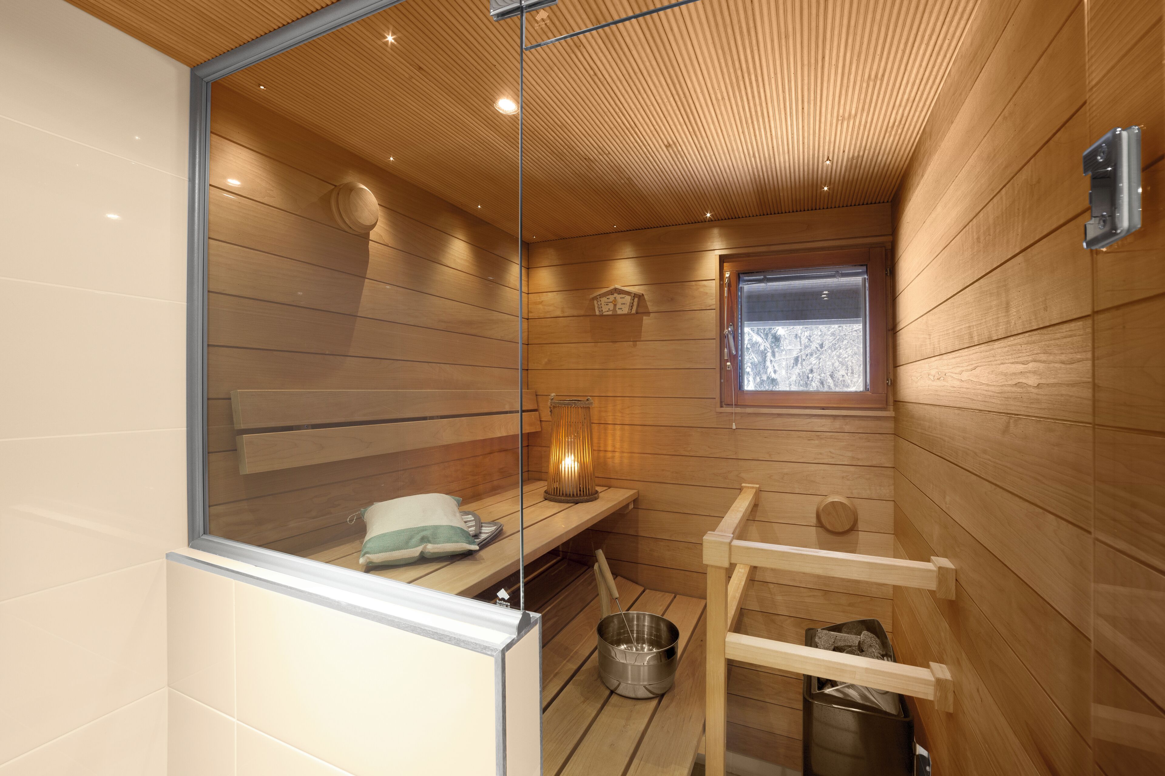 Un sauna avec des murs en bois, une fenêtre, un banc, un porte-serviettes et un seau en métal.