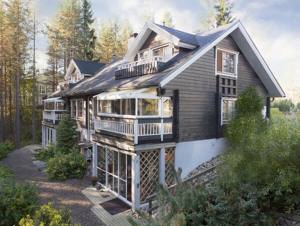 A two-story house with a balcony, a deck, and a view of the surrounding forest.