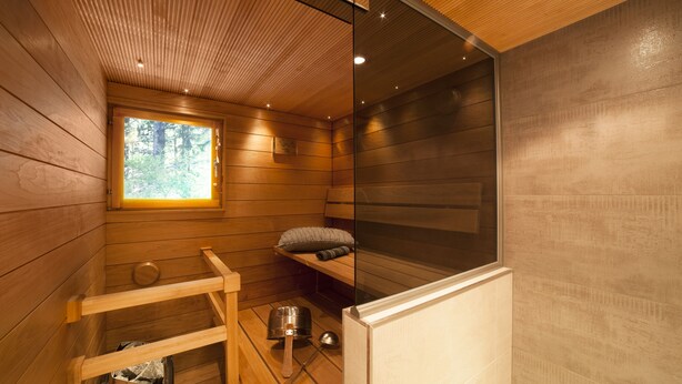 A sauna room with wooden walls, a window, a shelf with towels, and a small trash bin. - Vuokatin Aateli Studios (Sotkamo)