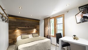 A bedroom with a wooden headboard, a bed with a beige bedspread, a desk with a chair, and a window with curtains. - Vuokatin Aateli Studios (Sotkamo)