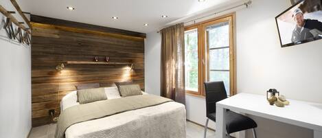A bedroom with a wooden headboard, a bed with a beige bedspread, a desk with a chair, and a window with curtains.